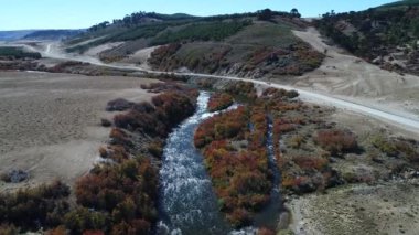 Litran Nehri hava dron sahne. Renkli Sonbahar bitki örtüsü riverbend ve araucarian woods, kamera çakıl yol yol nehir üzerinde hareket eder. Van yolu geçer. Villa Pehuenia - Moquehue. Patagonya Arjantin.