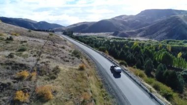 Bozkır, dağlar, ağaçlar ve yol ve bir izleme van ve yakaladığında bir römork hava dron sahne. Kamera hareketli ileriye.