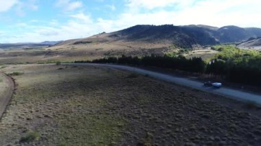 Bozkır, dağlar, ağaçlar ve yol ve bir izleme van ve yakaladığında bir römork hava dron sahne. Kamera hareketli ileriye.