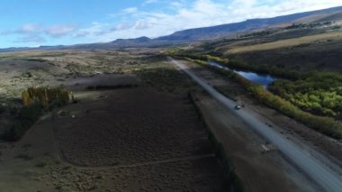 Bozkır, dağlar, ağaçlar ve yol ve bir izleme van ve yakaladığında bir römork Pulmari nehrin sağ ile hava dron sahne. Kamera hareketli ileriye.