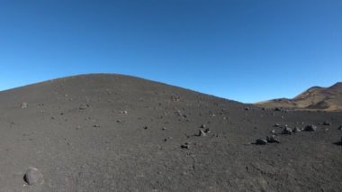 Fotoğraf makinesi kaydırma, La Payunia Milli Parkı, Malargue, yaptı. Siyah ve kırmızı dağlar ve volkanlar. Çakıl yol. Lapillis altın otlar ile volkanik kayalar. Payun Liso volkan arka plan üzerinde. 