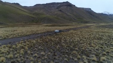 Andes Dağları, Mendoza, Arjantin hava dron sahne. Patagonya bozkır manzara. İleriye kamera. Yalnız yol izleme van römork, kamyonet ve karavan ile çakıl. Campanario dağın karla. Bulutlu karanlık gün.