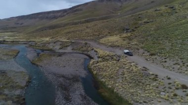 Andes Dağları, Mendoza Cuyo Arjantin hava dron sahne. Patagonya bozkır manzara. Kamera bir van römork, kamyonet ve karavan ile doğru bir tezcan nehir üzerinde geriye doğru gidiyor. Campanario dağın karla arka planda. Bulutlu karanlık gün.