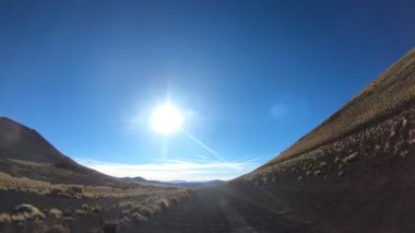 Timelapse, La Payunia Milli parkta Malargue, Cuyo, Mendoza. Çakıl siyah volkanik yol kayalar ve altın otlar üzerinde ilerlemeye araba, kamera kavradı. Volkanlar arka plan üzerinde.
