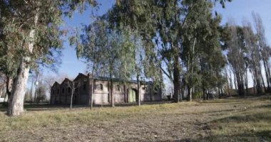 Seyahat ve panning kamera hareket vasıl günbatımı altın saat büyük tuğla inşaat mükemmel. Önünde uçan böcekler ya da fotoğraf makinesi. Ağaçlar, yapraklar ve çim. Kiler Mendoza, Arjantin şarap üretimi için.