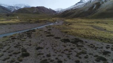 Andes Dağları, Mendoza Cuyo Arjantin hava dron sahne. Patagonya bozkır manzara. Kameranızın tezcan nehrine doğru birkaç at üzerinde yıldız koşma iletir. Campanario dağın karla arka planda. Bulutlu karanlık gün.