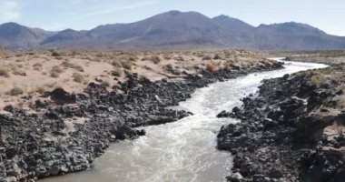 Rio Grande Nehri, mendoza cuyo, Arjantin. Kırmızı su akan lav rock soğuk siyah yatak arasında. Yan ve arka planda dağlar üzerinde kum.