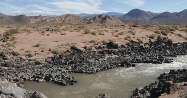 里奥格兰德河 门多萨 Cuyo 阿根廷 红水在熔岩岩石的冰冷的黑色床之间流动 背景上的沙滩和山上的沙子 — 图库视频影像