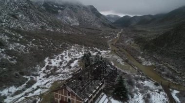 Hava dron sahne yapı, eski yanık otel Tunuyan Nehri Vadisi karlı gri gün yok. Kamera konstrüksiyon metal çatısı taşır. Karlı dağlar ve arka plan, bitki örtüsü