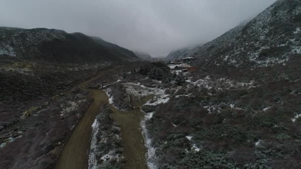 トゥヌヤン川と砂利道 背景でやけどを負った建設と雪渓の空中ドローン シーン 曇りの寒い冬の日 カメラは 建物に向かって移動します バジェ アルゼンチン — ストック動画