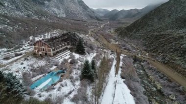 Hava dron sahne yapı, eski yanık otel karlı gri gün yok. Kamera İnşaat ve havuz bahçesinde genel görünümünü gösteren yükselir. Arka plan, Nehir vadi ve karlı dağlar