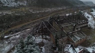 Hava dron sahne yapı, eski yanık otel Tunuyan Nehri Vadisi karlı gri gün yok. Kamera senital görüntü için hareket ediyor. Çıplak metal çatı yapısı. Karlı dağlar, arka plan, bitki örtüsü