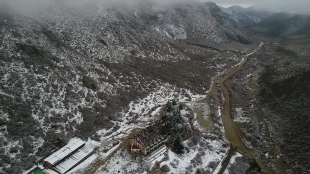 空中ドローンのシーンはトゥヌヤン川にある渓谷で灰色の雪の日に燃やされたホテルの建物は 古いを破壊しました カメラは裸鉄屋根近くの建設パスに向かって下る 背景の雪山 — ストック動画