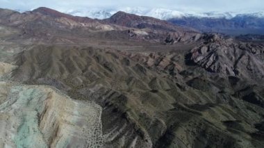 Seyahat ve kumlu erozyona uğramış dağlardan inen hava dron sahne. Arka plan karlı Andes Dağları. Bulutlu gizemli gün. Uspalllata, Mendoza, Argentina