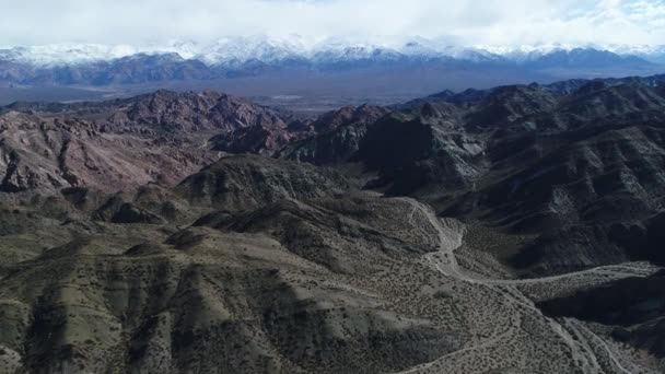 Luchtfoto drone scène reizen over zandige geërodeerde bergen. Snowy Andes-gebergte op de achtergrond. Bewolkt mysterieuze dag. Uspalllata, Mendoza, Argentinië — Stockvideo