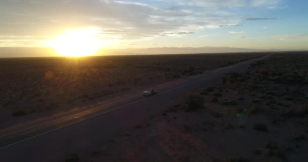 Escena aérea de dron de furgoneta con casa remolque en la ruta, en el Parque Nacional Talampaya, La Rioja, Cuyo Argentina. Hora dorada del atardecer. Sol en el horizonte. Montañas en el paisaje de fondo . — Vídeo de stock