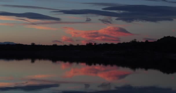 Espejo de paisaje escena oscura de puesta de sol hora dorada y reflejos de nubes en el agua moviéndose suavemente con pequeñas olas. Camping en La Rioja, Cuyo, Argentina . — Vídeos de Stock