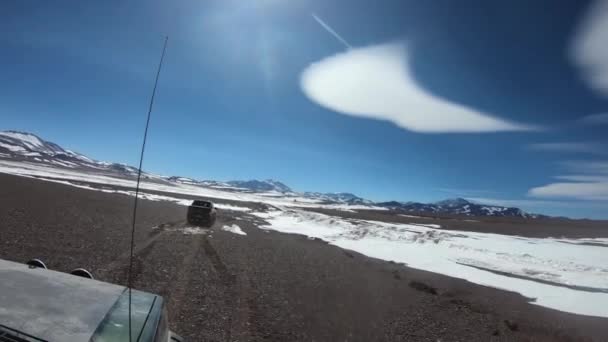 4x4 van fuera de la carretera, otro coche en la parte delantera. Paisaje negro, oscuro, rocoso, nevado con montañas y volcanes con nieve de fondo. Excursión Laguna Brava, Provincia de Rioja — Vídeo de stock