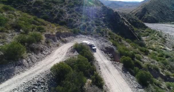 Escena aérea de dron de furgoneta con remolque, viajando por carretera de grava descendiendo ladera de las montañas Famatina. La cámara sigue al 4x4 moviéndose hacia atrás. Valles y colinas al fondo . — Vídeo de stock
