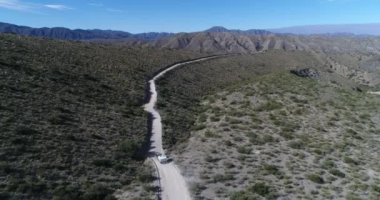 Çakıl yol Famatina Dağları, tepeleri üzerinde hava dron sahne Van römork, kamyonet ve karavan, ile seyahat. Kamera Monte xerophile bitki örtüsü, yatay görünümünü araba izler. 4 x 4 macera izle
