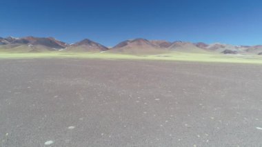 Hava dron sahne önünde sarı bitki örtüsü ile kayalık erozyona uğramış renkli dağların. Catamarca, Arjantin. Manzara genel bakış. Geriye doğru uçan.
