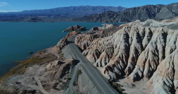 Escena aérea de drones de lago azul y montañas erosionadas con ríos secos y barrancos. Camino a lo largo de la costa arenosa con vegetación adaptada a las condiciones salinas. Presa Cuesta del Viento, provincia de San Juan — Vídeo de stock