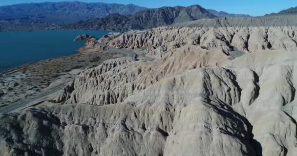 Légi drone jelenet kék-tó és a száraz folyók és vízmosások erodált hegyek. A homokos tengerpart mentén út. Utazás dombokon. Cuesta del Viento gát, San Juan megye — Stock videók