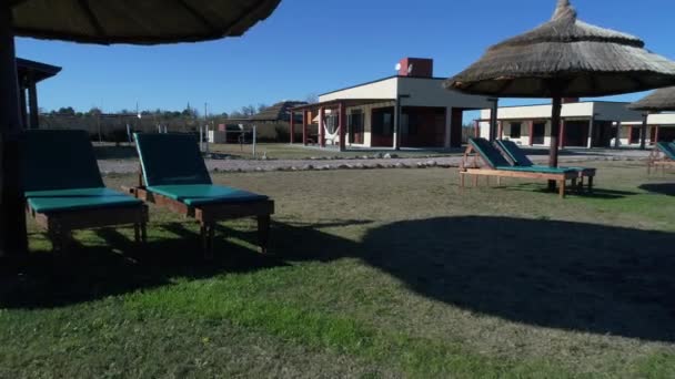 Aerial drone scene of straw umbrellas and beach chairs at a private hotel park. Camera moves forwards towards construction. Touristic Spa area. San Rafael, Mendoza, Argentina — Stock Footage Aerial Drone Scene Straw Umbrellas Beach Chairs Private Hotel Park Video Clip