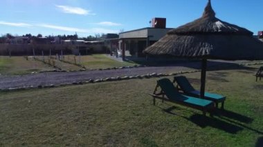 Plaj sandalyeleri ve otelin özel park hasır şemsiyeler hava dron sahne. Cottages adlı arka plan. Sandalye ile kamera başlar inşaat doğru ileri gider. Turistik alan. San Rafael, Mendoza