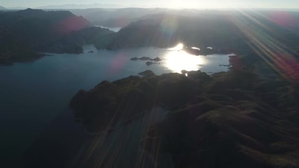 日落时山间巨大湖泊的空中无人机场景 耀斑和体积灯 在水面上向后飞行 雷尤诺斯水电大坝 背景山的自然的 Silhuettes — 图库视频影像