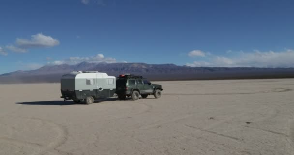 Autocaravana, caravana con furgoneta en el barro. Cámara de mano acercándose al remolque con coche de aventura 4x4 en el paisaje desértico seco. Montañas al fondo. Leoncito, Provincia de San Juan, Argentina — Vídeo de stock