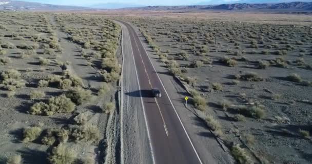 Luchtfoto drone scène van auto reizen over de weg in de vallei van de rivier tussen geërodeerde zanderige heuvels. Zonsondergang tijd. Calingasta, San Juan, Argentina. — Stockvideo