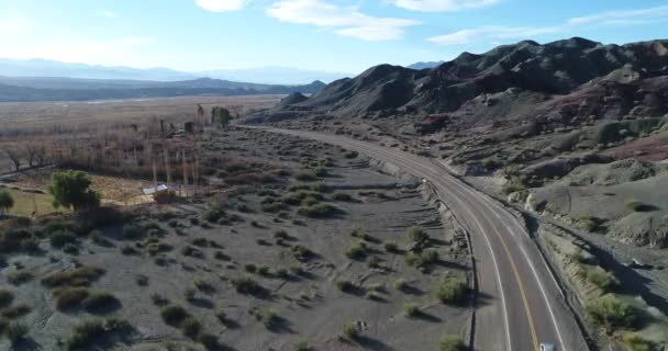 Escena aérea de drones de coche que viaja por carretera en el valle del río entre colinas arenosas erosionadas. Hora del atardecer. Calingasta, San Juan, Argentina . — Vídeos de Stock