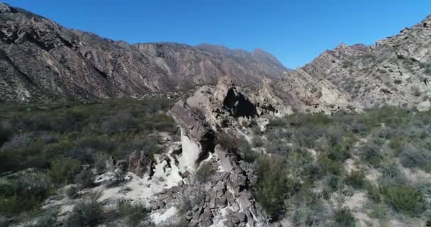 Сцена воздушного беспилотника из сухой долины и сложенных гор. Летают над скалами. Малая местная растительность покрывает низкие регионы. Провинция Сан-Хуан, Уако, Аргентина — стоковое видео