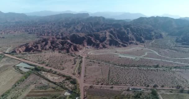 Escena aérea de aviones no tripulados de montañas plegadas erosionadas rojas. Moviéndose a lo largo de las construcciones de suburbios hacia formaciones geológicas secas. Villa Union, provincia de Rioja, Argentina — Vídeo de stock