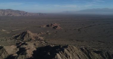 Kuru desertic dağlık manzara havadan dron sahne. Erozyona uğramış kayalık oluşumlar üzerinde uçan geniş pampa kuru nehirler tarafından çizilmiş. Puslu dağ zincirleri, arka plan. Castelli, Rioja Eyaleti, Arjantin