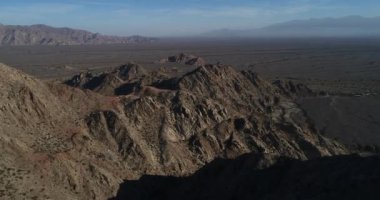 Kuru desertic dağlık manzara havadan dron sahne. Erozyona uğramış kayalık oluşumlar üzerinde uçan geniş pampa kuru nehirler tarafından çizilmiş. Puslu dağ zincirleri, arka plan. Castelli, Rioja Eyaleti, Arjantin