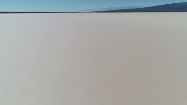 Escena aérea de drones del árido desierto seco de barreal en aimogasta, la rioja, Argentina. Cámara avanzando rápidamente cerca del suelo a una tierra vacía llena de pistas de coche. Montañas en el fondo . — Vídeo de stock