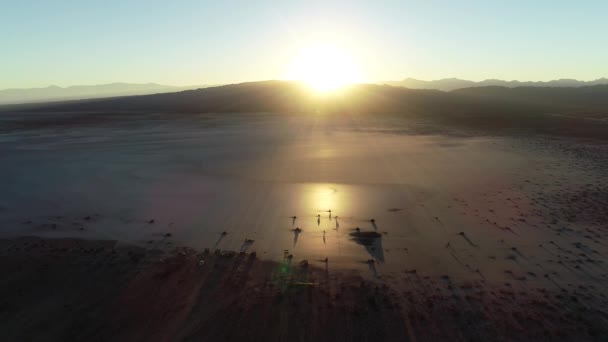 Drohnen-Szene bei Sonnenuntergang. Sonnenreflexion über der flachen Wüste. Kamera bewegt sich in Richtung Silhouetten von Konstruktionen. barreal de arauco, aimogasta, rioja provinz, argentinien — Stockvideo