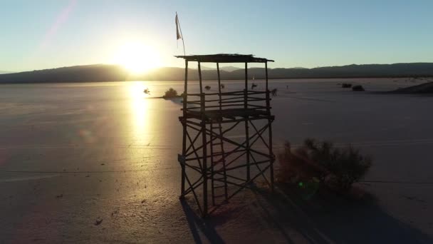 Letecká drone scéně sillhuete dřevěná rozhledna na rovině poušť, slunce. Zlaté hodiny slunce se odráží šplhat povrchu Barreal de Arauco, Rioja Province, Argentina. Infraestructure auto plachta — Stock video