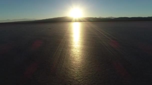 Antenn drönare scen flygande mot horisonten vid solnedgången i torr skinande bruten mark. Solen reflekterar över Miga yta. Barreal de Arauco, Aimogasta, Rioja provinsen, Argentina — Stockvideo