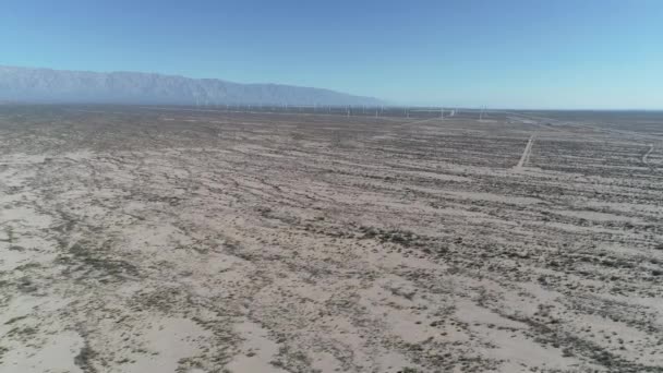 Escena aérea de drones de campo de viento lleno de aerogeneradores en Aimogasta, la rioja, Argentina. Generación de energía verde clara sostenible. Cámara subiendo y bajando. Las montañas de los andes en el fondo . — Vídeo de stock