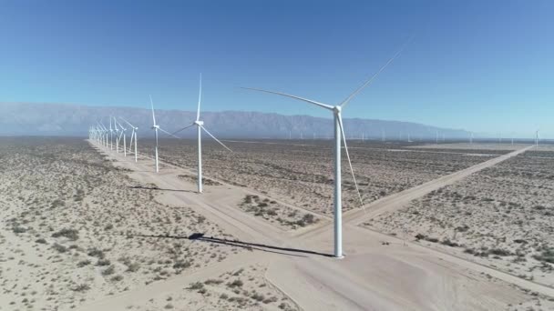 Сцена воздушного беспилотника с ветровым полем, полным выровненных ветряных турбин в Аймогасте, ла-Риоха, Аргентина. Поколение экологически чистой зеленой энергии. Камера движется влево. Горы на заднем плане . — стоковое видео