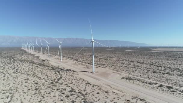 Escena aérea de drones de campo de viento lleno de aerogeneradores alineados en Aimogasta, la rioja, Argentina. Generación de energía verde clara sostenible. Cámara en el futuro. Las montañas de los andes en el fondo . — Vídeos de Stock