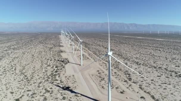 Cena de drones aéreos de campo de vento cheio de turbinas eólicas alinhadas em Aimogasta, la rioja, Argentina. Geração de energia limpa verde sustentável. A câmara vai para cima e para trás. Montanhas no fundo . — Vídeo de Stock