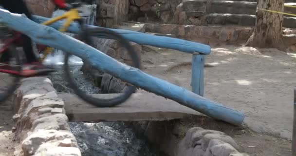 Detalle de ruedas de bicicleta lanzando brige de hormigón sobre un pequeño canal, conducto como un pequeño río con agua en una carrera de bicicletas en Londres, Provincia de Catamarca, Argentina . — Vídeos de Stock