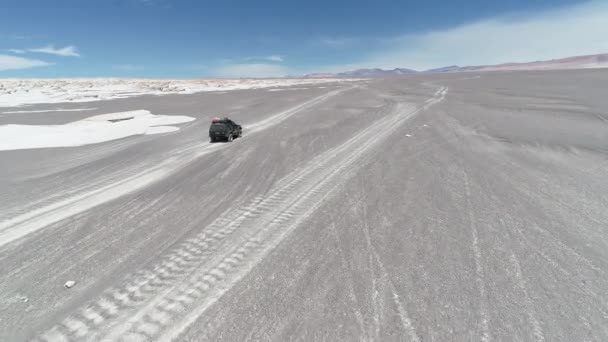 Escena aérea del dron del coche conduciendo fuera de la carretera en el desierto gris entre las esturcturas rocosas naturales blancas del campo de pómez. Montañas grises al fondo. Antofagasta de la Sierra, Catamarca, Argentina — Vídeo de stock
