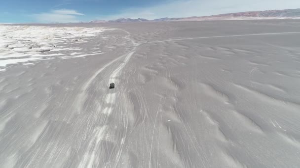 Escena aérea de furgoneta 4x4 conduciendo fuera de la carretera en suelo arenoso gris desértico junto a amplio paisaje volcánico de campo pómez. Paisaje seco colorido. Vista descendente, general. Catamarca, Argentina — Vídeo de stock