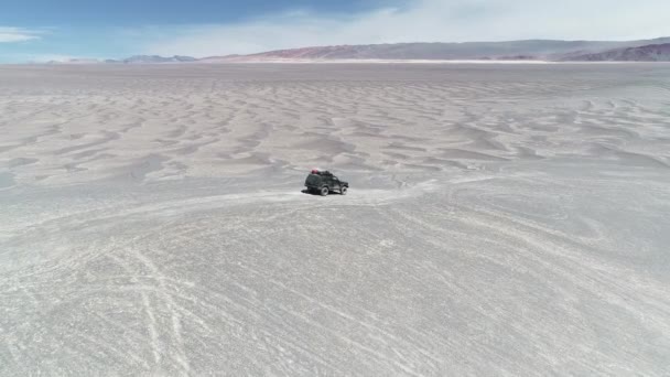 在灰色沙漠上驾驶一辆远征面包车离开公路后的空中无人机场景。侵蚀的五颜六色的山在背景。Antofagasta de la Sierra, Catamarca, Argentina — 图库视频影像