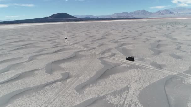 オフロード砂漠の火山地域における砂の砂丘の間運転 2 台のバンの空中シーンは。背景に壮大な黒 Carachi パンパにある火山。不毛の風景に遠征。カタマルカ、アルゼンチン — ストック動画